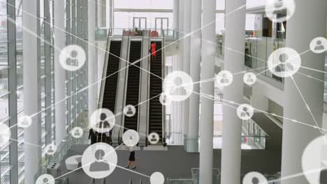 Animation-of-network-of-profile-icons-over-aerial-view-of-escalators-at-modern-office