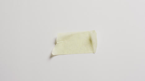 Video-of-close-up-of-torn-piece-of-yellow-paper-on-white-background