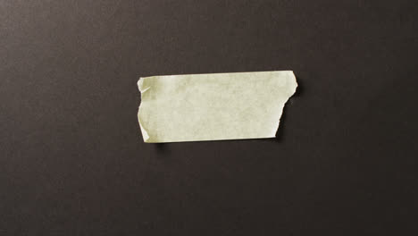 Video-of-close-up-of-yellow-paper-tape-piece-on-black-background