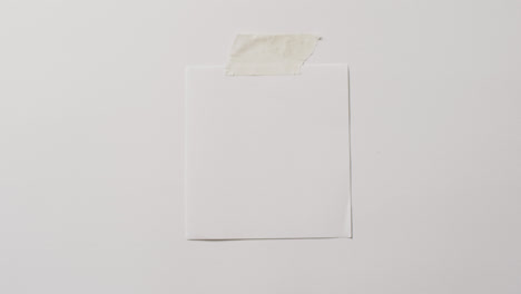 Video-of-close-up-of-white-memo-note-with-copy-space-taped-to-white-background