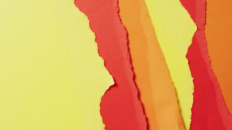 Video-of-close-up-of-torn-pieces-of-yellow,-red-and-brown-paper-background