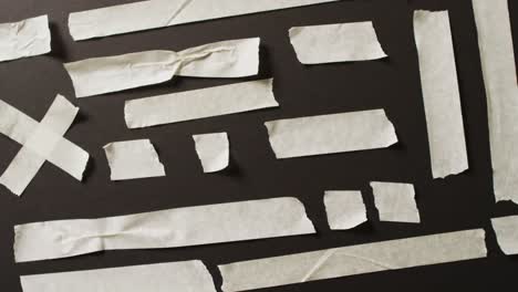 Video-of-close-up-of-multiple-white-paper-tape-pieces-on-black-background