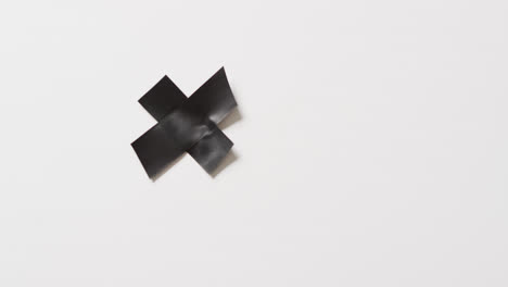 Video-of-close-up-of-black-tape-forming-cross-on-white-background