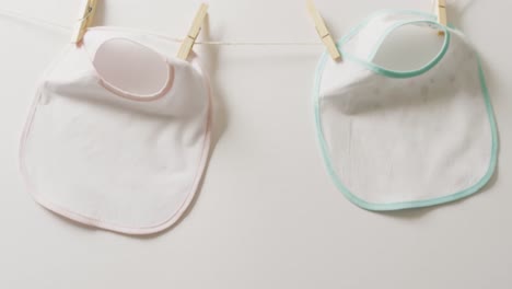 Video-of-close-up-of-two-white-baby-bib-with-pegs-hanging-on-white-background