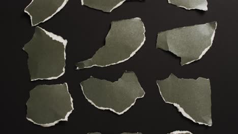 Video-of-close-up-of-multiple-torn-piece-of-green-paper-on-black-background