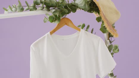 Video-of-close-up-of-white-t-shirt-hanging-on-purple-background