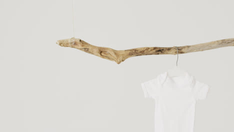 Video-of-close-up-of-white-baby-grow-hanging-from-branch-on-white-background