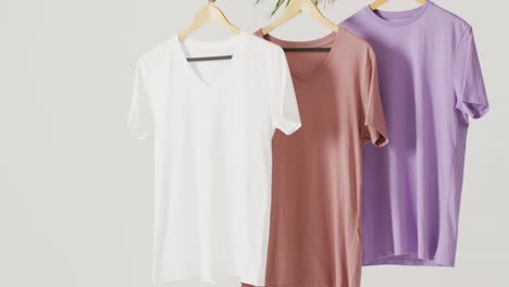 Video-of-close-up-of-white,-beige-and-purple-t-shirts-hanging-on-white-background