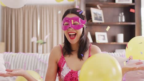 Video-of-smiling-biracial-woman-in-pink-party-mask-and-dressed-in-pink-dress