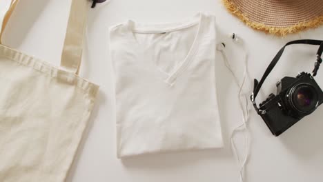 Video-of-close-up-of-white-t-shirt,-bag,-sunhat,-earphones-and-camera-on-white-background