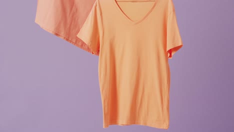 Video-of-close-up-of-orange-t-shirts-hanging-on-purple-background