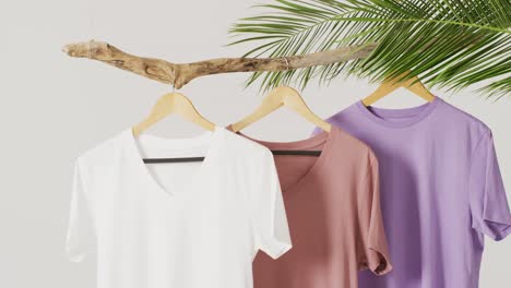 Video-of-close-up-of-white,-beige-and-purple-t-shirts-hanging-on-branch-on-white-background