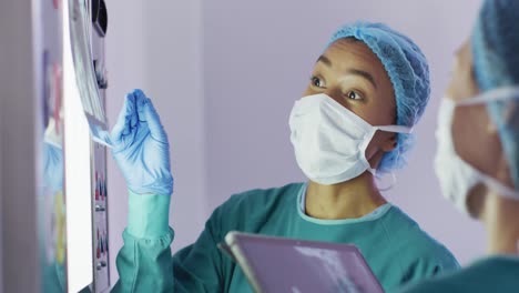 Video-Einer-Birazialen-Chirurgin,-Die-Mit-Einer-Kollegin-Im-Operationssaal-über-Röntgenaufnahmen-Spricht