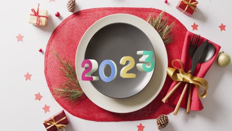 Animation-of-2023-text-and-christmas-place-setting-and-decorations-in-background