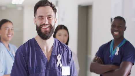 Video-portrait-of-happy-caucasian-male-doctor-with-cancer-ribbon-in-hospital-corridor,-copy-space