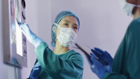 Video-Einer-Asiatischen-Chirurgin,-Die-Mit-Einer-Kollegin-Im-Operationssaal-über-Röntgenaufnahmen-Spricht
