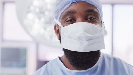 Video-portrait-of-african-american-male-surgeon-wearing-face-mask-in-operating-theatre,-copy-space