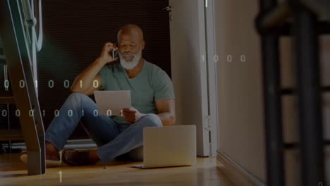 Animation-of-binary-coding-over-african-american-man-holding-document-talking-on-smartphone-at-home