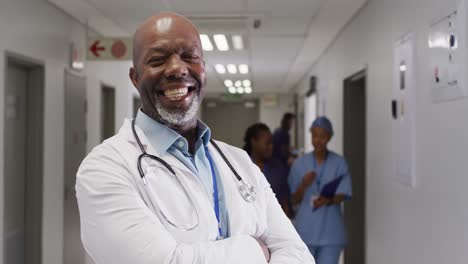 Video-portrait-of-smiling-senior-african-american-male-doctor-in-busy-hospital-corridor,-copy-space