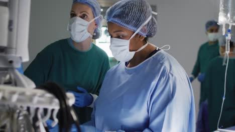 Video-of-two-diverse-female-surgical-assistants-preparing-electronic-equipment-in-operating-theatre
