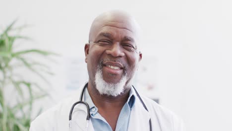Video-portrait-of-happy-senior-african-american-male-doctor-smiling-in-hospital-corridor