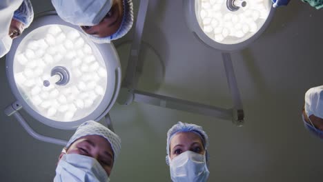 Video-of-patient-view-looking-up-at-diverse-group-of-surgeons-and-lights-in-operating-theatre