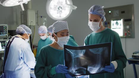 Video-Von-Zwei-Verschiedenen-Chirurginnen,-Die-Im-Operationssaal-über-Röntgenaufnahmen-Diskutieren