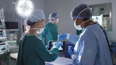 Video-Von-Zwei-Unterschiedlichen-Chirurginnen,-Die-Im-Operationssaal-über-Röntgenaufnahmen-Auf-Einem-Tablet-Diskutieren