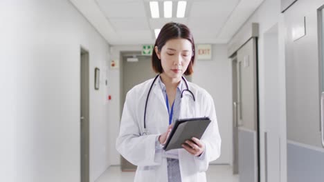 Video-Einer-Asiatischen-Ärztin,-Die-Durch-Den-Krankenhauskorridor-Geht,-Auf-Das-Tablet-Schaut,-Platz-Zum-Kopieren