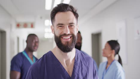Video-portrait-of-smiling,-bearded-caucasian-male-medical-worker-in-busy-hospital-corridor