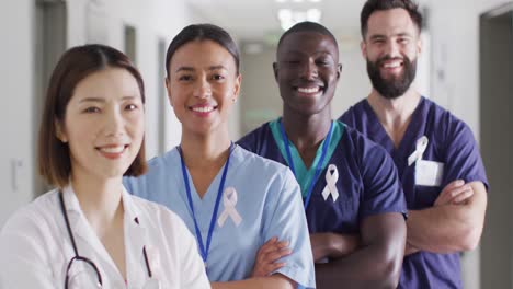 Video-portrait-of-diverse-group-of-smiling-medical-workers-with-cancer-ribbons-in-hospital-corridor