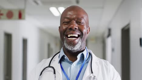 Retrato-En-Video-De-Un-Feliz-Y-Senior-Médico-Afroamericano-Riéndose-En-El-Pasillo-Del-Hospital