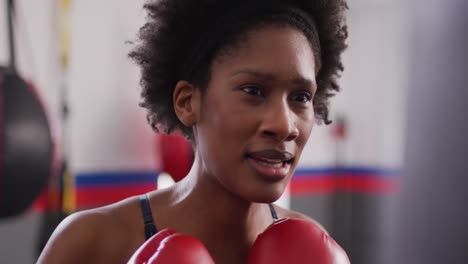 Video-Einer-Selbstbewussten,-Entschlossenen-Afroamerikanischen-Frau-In-Boxhandschuhen,-Die-Im-Fitnessstudio-Mit-Boxsack-Trainiert