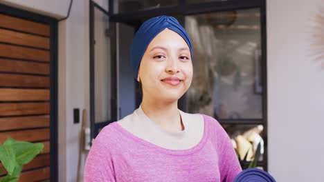 Video-portrait-of-happy-biracial-woman-in-blue-hijab-smiling-to-camera-in-living-room-at-home