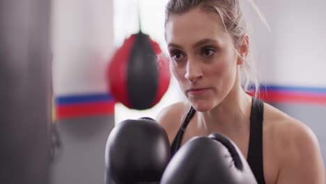 Video-Einer-Selbstbewussten,-Entschlossenen-Kaukasischen-Frau-In-Boxhandschuhen,-Die-In-Einem-Fitnessstudio-Mit-Einem-Boxsack-Trainiert