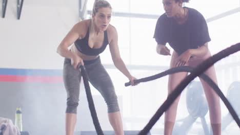 Video-of-diverse-female-fitness-trainer-encouraging-woman-battling-ropes-working-out-at-a-gym