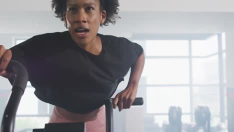 Video-Einer-Entschlossenen-Afroamerikanischen-Frau-Auf-Dem-Heimtrainer,-Die-In-Einem-Fitnessstudio-Trainiert