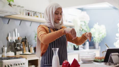 Video-Einer-Glücklichen-Gemischtrassigen-Frau-Im-Hijab,-Die-In-Der-Küche-Backt,-Mehl-Streut-Und-Ein-Tablet-Verwendet