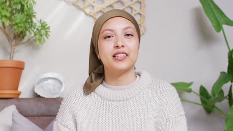Video-of-happy-biracial-woman-in-hijab-making-video-call-talking-to-camera-at-home