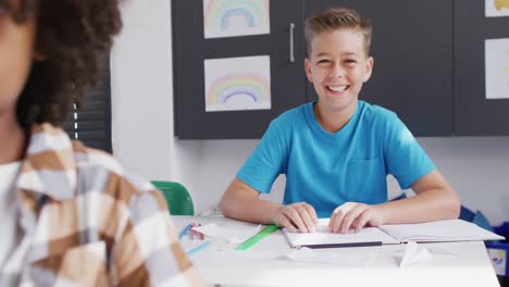 Portrait-of-happy-caucasian-schoolboy-smiling-at-desk-in-classroom