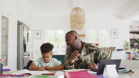 Glücklicher-Afroamerikanischer-Soldat-Und-Sein-Sohn-Sitzen-Am-Tisch,-Arbeiten-Und-Machen-Hausaufgaben