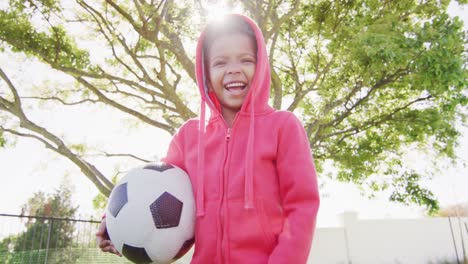 Retrato-De-Un-Niño-Afroamericano-Feliz-Sosteniendo-Fútbol-En-El-Jardín