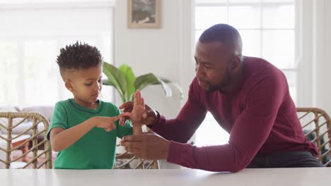 Happy-african-american-man-and-his-son-sitting-at-table-and-speaking-sign-language