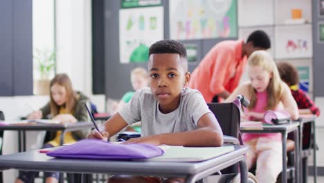 Portrait-of-happy-diverse-schoolchildren-at-desks-writing-in-school-classroom