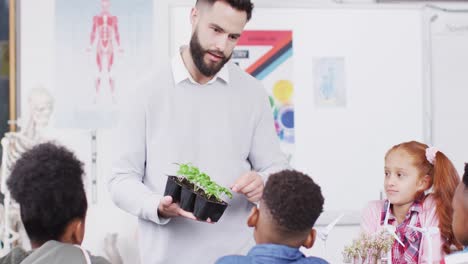 Diverse-male-teacher-and-happy-schoolchildren-studying-plants-in-school-classroom