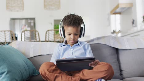 Glücklicher-Afroamerikanischer-Junge,-Der-Auf-Dem-Sofa-Sitzt-Und-Ein-Tablet-Benutzt