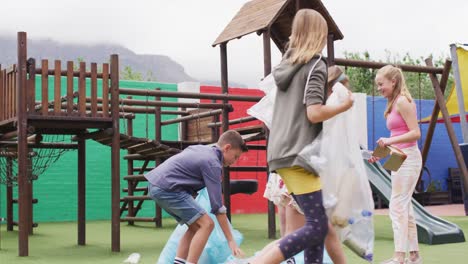 Happy-caucasian-schoolchildren-cleaning-together-with-bags-at-school-playground
