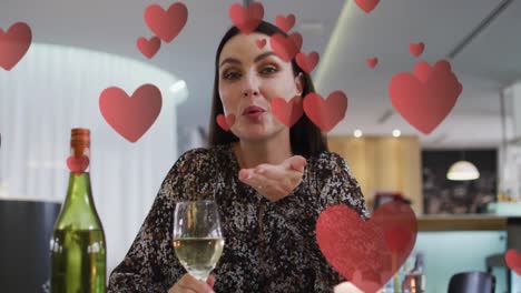 Animation-of-hearts-over-caucasian-woman-drinking-wine-and-having-video-call
