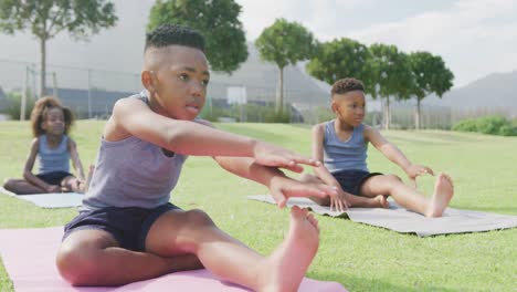 Video-of-three-african-american-schoolchildren-practicing-yoga-sitting-in-outdoor-class