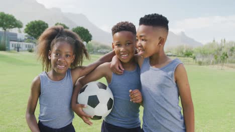 Retrato-En-Video-De-Tres-Niños-Afroamericanos-Felices-Sosteniendo-Fútbol-En-El-Campo-Escolar